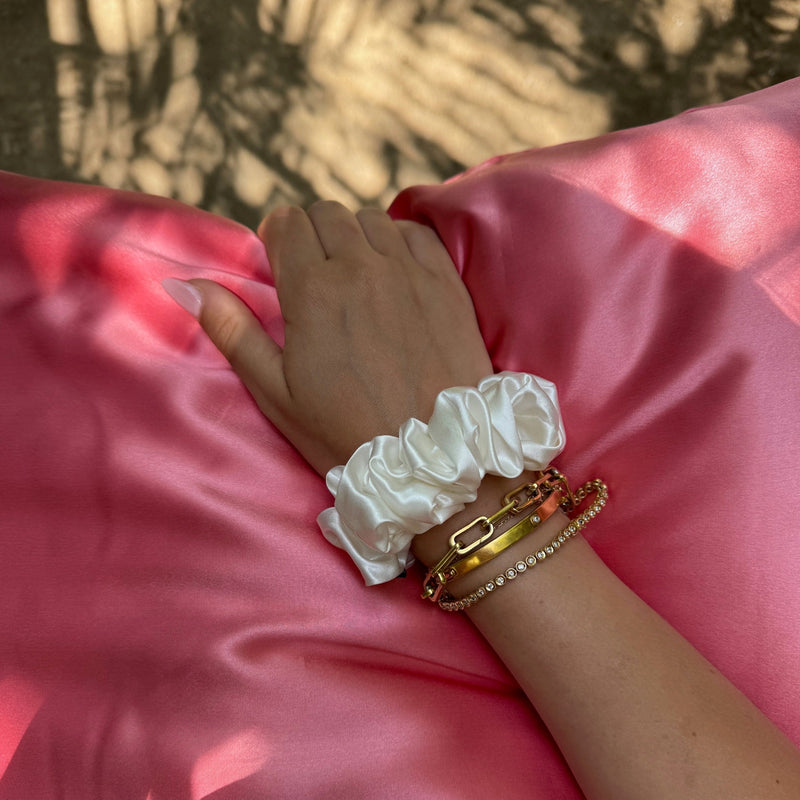 Large ivory silk scrunchie on wrist of a lady whose hand is on top of a mulberry silk watermelon pillowcase.