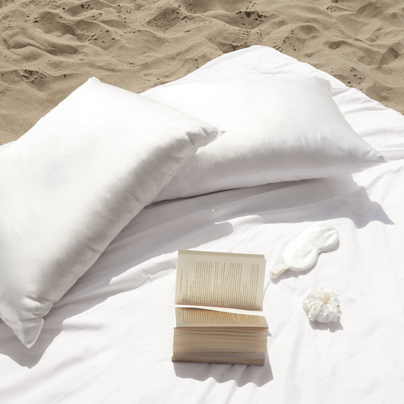 Two ivory mulberry silk pillowcases on the beach with a silk sleep mask.