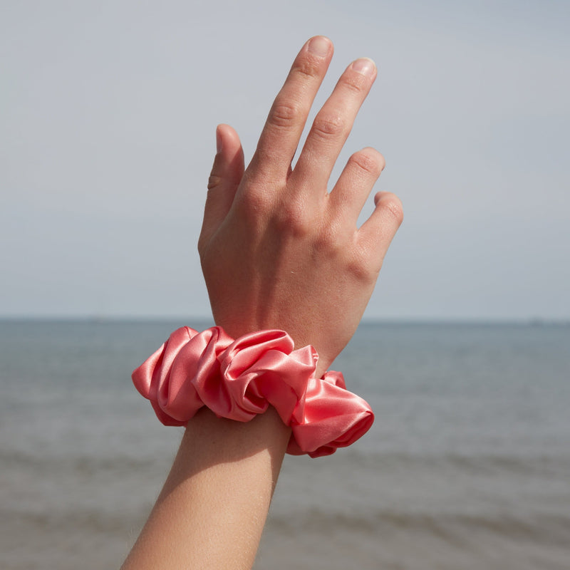 A hand with a large watermelon coloured silk scrunchie on her wrist.