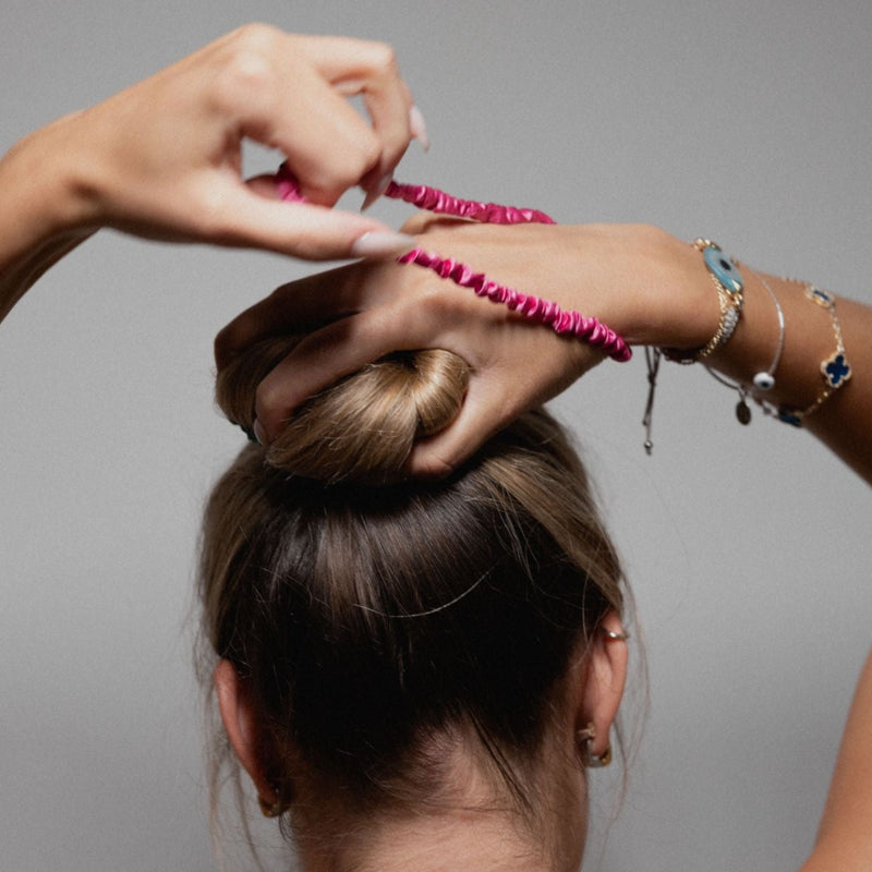 Lady tying her hair up with a slim silk scrunchie.