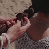 Video of a lady plaiting her hair and tying it with a large green silk scrunchie. The lady is also wearing white silk skinny scrunchies on her wrist.